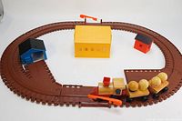 Full layout of vintage 1972 Mattel wooden train set on brown oval track with three small buildings (yellow, blue, red) and wooden locomotive and passenger cars covered with spherical wooden passengers.