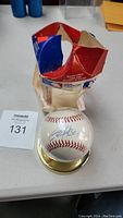 Signed baseball inside a clear holder with gold-plated pedestal alongside the original MLB box which is slightly crushed.