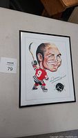 Front view of framed signed caricature of Bobby Hull, showing caricatured image of Bobby Hull in red hockey uniform with number 9 and large head, holding hockey stick. Signature visible at bottom right.