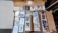 Open boxes filled with thousands of mixed sports trading cards including hockey, baseball, and basketball.
