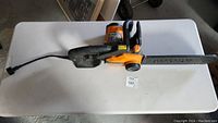 Full view of the Worx electric chainsaw laid flat on a white table, showing the body, handle, and 16-inch blade with chain cover attached.
