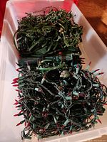 Large plastic bin filled with tangled white and multicolored Christmas light strands and light webs with green wiring.