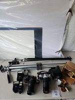 Overview of all items on table including cameras, flash units, tripods, poster boards, and accessories