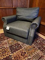 Gray upholstered chair with rolled arms and nailhead trim shown from front