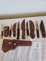 Full set of hunting knives laid out with their respective leather sheaths and a large leather gun holster