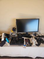 Wide view of all items on table including Dell monitor, Wii console and accessories, gaming controllers, headset, and multiple chargers and cables.