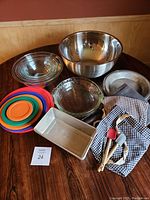 Photo showing entire lot on table including glass Pyrex bowls with lids, metal mixing bowl, pie plates, loaf pans, utensils and aprons.