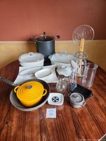 Full lot overview showing various cookware and serving pieces arranged on a round wooden table, including enamel pots, glass containers, and porcelain dishes.