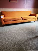 Full front view of bright orange mid century style couch with two seat cushions and slim metal legs.