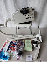Side view of Oreck XL hand vacuum on Costco step stool. Included on surface are vacuum hose parts, replacement belts, dust bags in original packaging, and instruction manual.