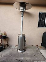 Full view of the tall stainless steel gas patio heater against an exterior wall showing its overall size and shape.