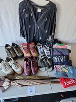 Photo showing multiple pairs of shoes in various brands and colors with clothing items folded on table and a folded umbrella.