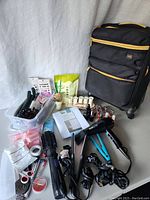 Full overview photo showing the black and yellow Lucas carry-on suitcase with multiple hair styling tools including blow dryers, flat irons, curlers, nail polish bottles, travel bottles, and bath items arranged on a tabletop.