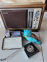 Front view of vintage Sony radio with dials, painted ceramic owl, vintage first aid kit, and vintage measuring tape.
