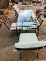 Overall view of the outdoor table with beveled glass top and wrought iron chairs with cushions on a concrete patio.