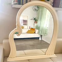 Front view of large sculpted postmodern cream ribbed frame mirror showing reflective surface and asymmetrical styling.