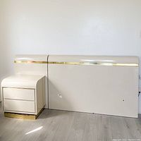 Full view of queen-size headboard and nightstand showing cream off-white laminate finish with gold accent panels.