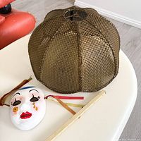 Lower angle view of the flower-shaped rattan pendant light shade sitting on a white table alongside a decorative mask.
