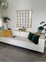 Side and angled view of white leather couch with yellow and green pillows, gold animal figurine on backrest, wall art behind.