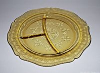 Close-up photo of a single amber depression glass plate with three compartments and ornate pressed glass pattern