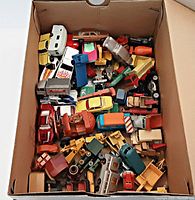 Top view of cardboard box filled with assorted vintage toy vehicles, various colors and types visible.
