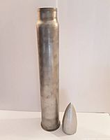 Full view of hollow metal cylinder and separate pointed metal top, showing size and shape