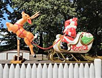 Side view of Santa in sleigh and reindeer on wooden stand against outdoor background