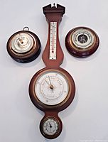 Front facing image showing the full lot of three vintage wood barometers: one large banjo-shaped Airguide barometer and two smaller round Stellar barometers.