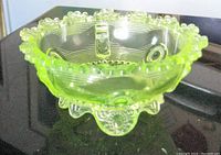 Vaseline glass bowl showing fluorescent yellow-green color with raised circular and floral edge details, ribbed sides and clear bottom