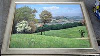 Framed oil painting depicting a scenic countryside landscape with trees, fields, and distant hills under a blue sky with clouds.