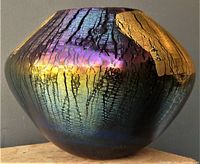 Front view of a signed Robert Eickholt volcano-inspired vase with iridescent black and gold foil surface.