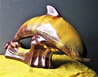 Front diagonal view of the dolphin statue on yellow cloth background, showing brown to yellow glaze transition and texture.