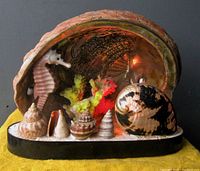 Photo showing the lamp front with large shell backdrop, white seahorse, colorful coral, and seashells on black base.