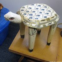 Photo of first enameled wooden accent table shaped like a turtle with painted details including blue shapes and gold accents on the shell and a detailed head with painted eyes.