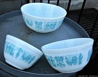 Three Pyrex mixing bowls displaying the Amish Butterprint turquoise and white pattern, arranged on metal surface