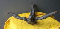Top view showing front of the cast-iron nude male flying man wall sculpture on a yellow cloth background.