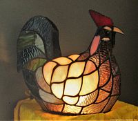 Front angle of stained glass chicken table lamp illuminated, showing its rooster comb detail and multi-colored glass pattern.