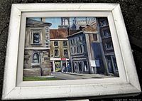 Framed oil painting of Old Quebec street scene in white frame with visible wear on frame edges.