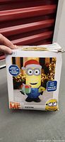 Box for 5 ft tall inflatable Kevin Minion from Despicable Me featuring the character with Santa hat and gift, showing front side of package.