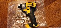 Side front view of Dewalt 20V Max impact driver on clear plastic wrap, showing ergonomic handle and trigger area.