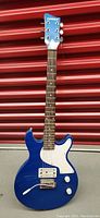 Front view of blue First Act electric guitar with white pickguard, two control knobs, single humbucker and single coil pickups, and vibrato bar.