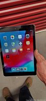 Front view of iPad Air showing home screen with app icons, held in hand against red backdrop.