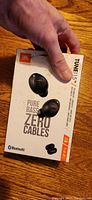 Front of box showing JBL Tune 115 earbuds, Pure Bass, Zero Cables, Bluetooth logos, and 21h battery life indicated