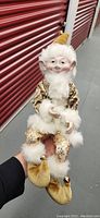Front view of the elf doll showing detailed face, white hair, patterned gold and cream outfit with fur trim, and pointed hat.