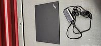 Closed Lenovo ThinkPad T14 laptop and power adapter laid flat