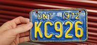 Front view of small vintage Ontario license plate from 1972, showing blue background with yellow characters 'ONT 1972 KC926'. Four mounting holes visible.