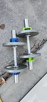 Two metal dumbbells on ground, each with 2 weight plates and quick change clips—one blue, one green.