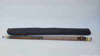 Full view of pool cue aligned next to the black soft padded carrying case