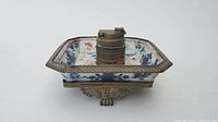 Top view showing square porcelain tray with intricate floral patterns and brass central ink container or lighter.