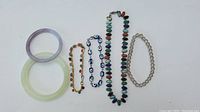 Photo of 2 jade bangles, 1 multi-colored bead necklace, and 3 bracelets (chain with stones, eye beads, and translucent beads)